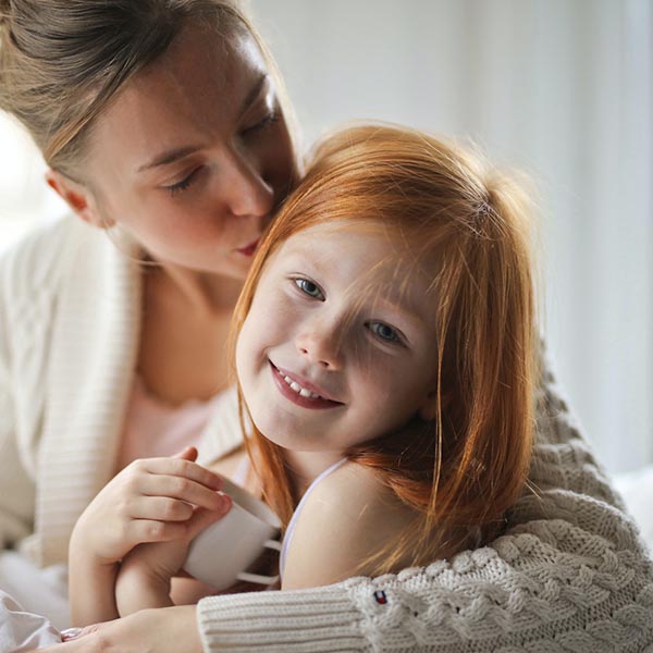 Mother kissing a smiling child on the top of her head during a hug, Andrea Piacquadio - Pexels.