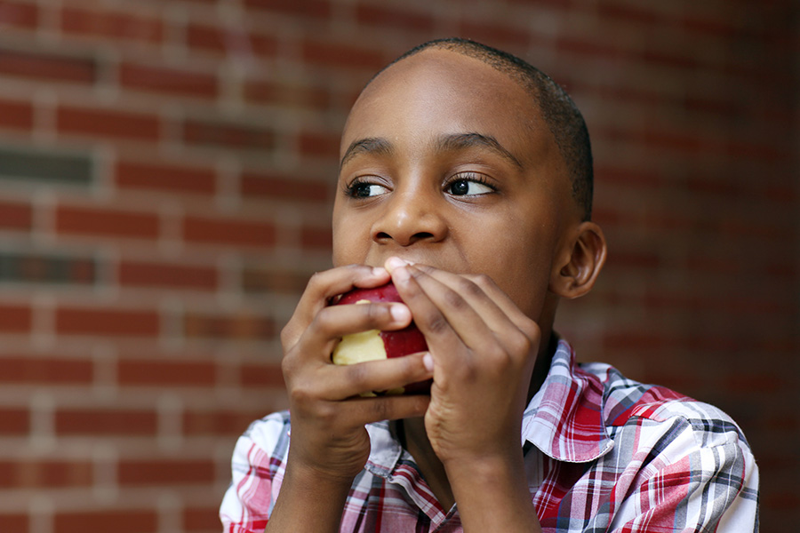 Adolescent boy eating red apple, by iStock.