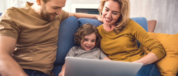 stock photo of mother and father sitting on couch with child looking at a laptop, smiling; credit: Canva