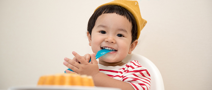 stock photo of hand holding a spoon full of pureed food, stretched towards a child's mouth; credit: Canva