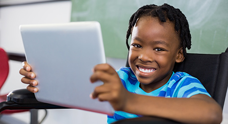 young child looking at the camera smiling, holding an iPad; credit: Shutterstock