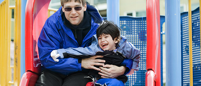 parent holding child on a slide on an outdoor playground; photo credit: iStock