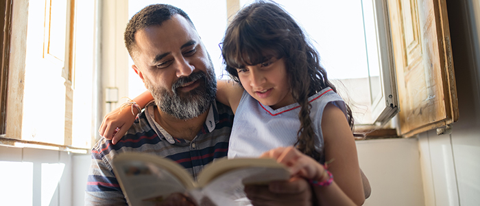 Man reading book to daughter beside an open window, credit Kampus Productions - Pexels.