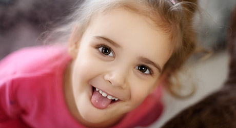 stock photo of young girl with big dark eyes, looking up at camera, playfully sticking out her tongue; credit: Adobe