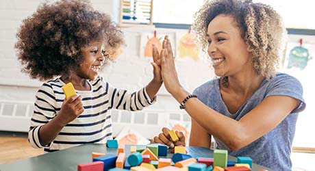 iStock photo: toddler girl smiling, playing blocks with and giving high-five to therapist