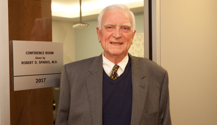 Robert Sparks, M.D., stands outside a conference room named in his honor inside the Harold M. and Beverly Maurer Center for Public Health at UNMC.