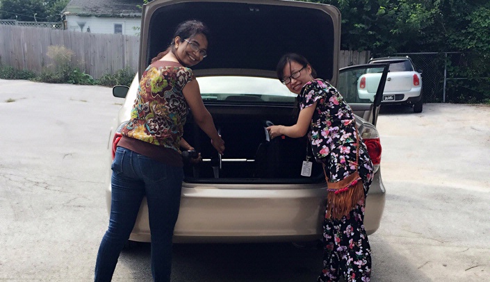 Graduate Student Association Board member Cheng Wang, right, helps a student load her car after the "houshold goods sale" for new international students in August. Donations are being sought for the new sale, to be held the first week in September.
