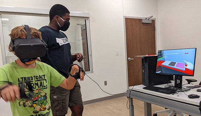 A camper plays a virtual reality video game as a counselor looks on at the HABIT camp held this summer at the Munroe-Meyer Institute.