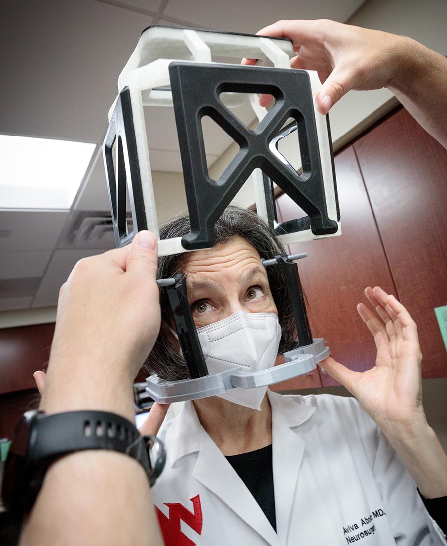 Aviva Abosch, MD, PhD, chair of the UNMC Department of Neurosurgery, dons the head frame and box models with help from Brian Maass.