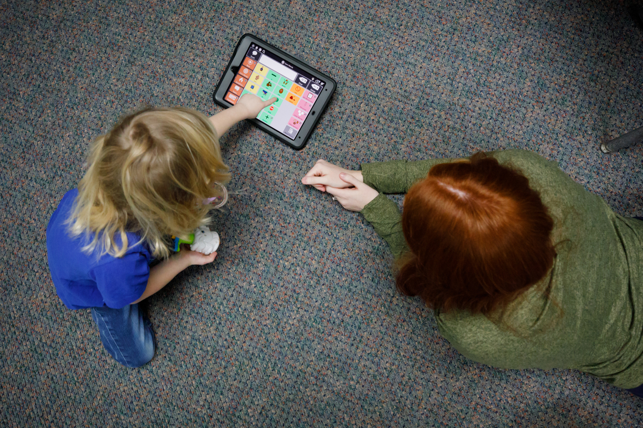 Hannah uses a portable touch-pad communicator to "talk" with her therapist.