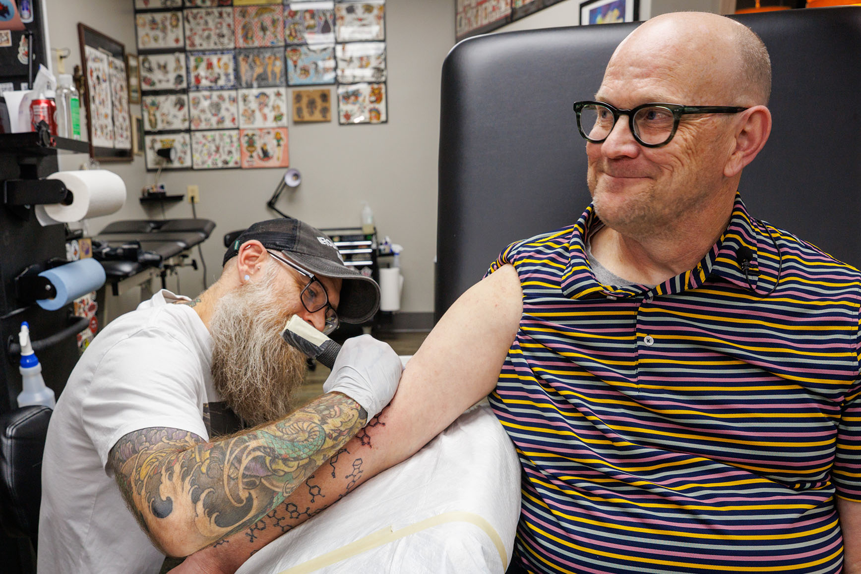 Corey Hopkins, PhD, interim chair of the department of pharmaceutical sciences, gets four new tattoos at Ironwood Ink Thursday May 1, 2025. If a student has a compound that makes it into animal testing, he has it tattooed on his arm. He currently has about 29.