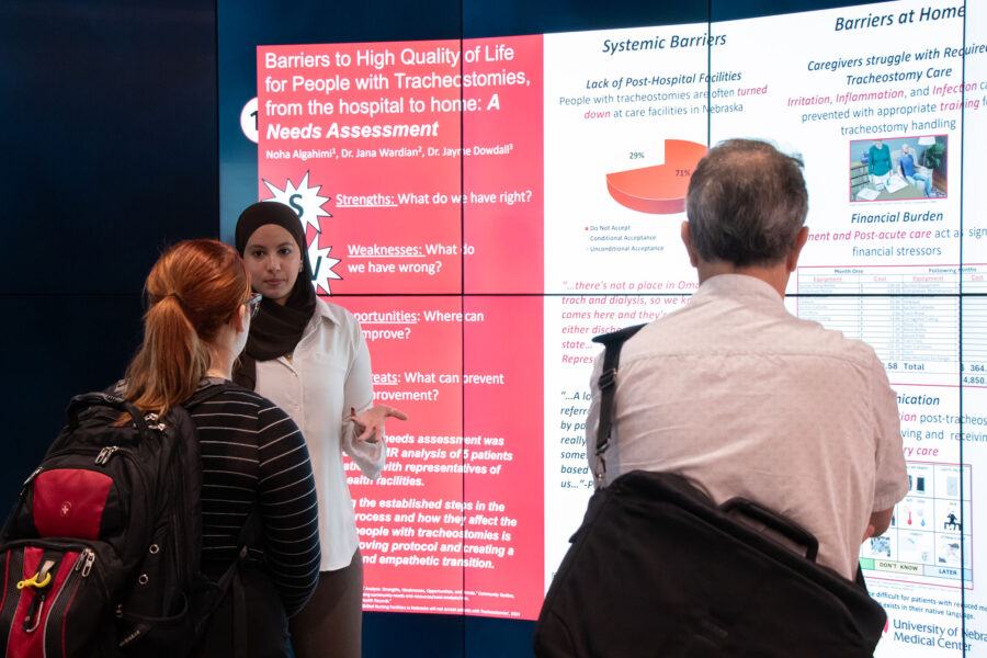 A medical student standing in front of a digital screen to present her research to attendees