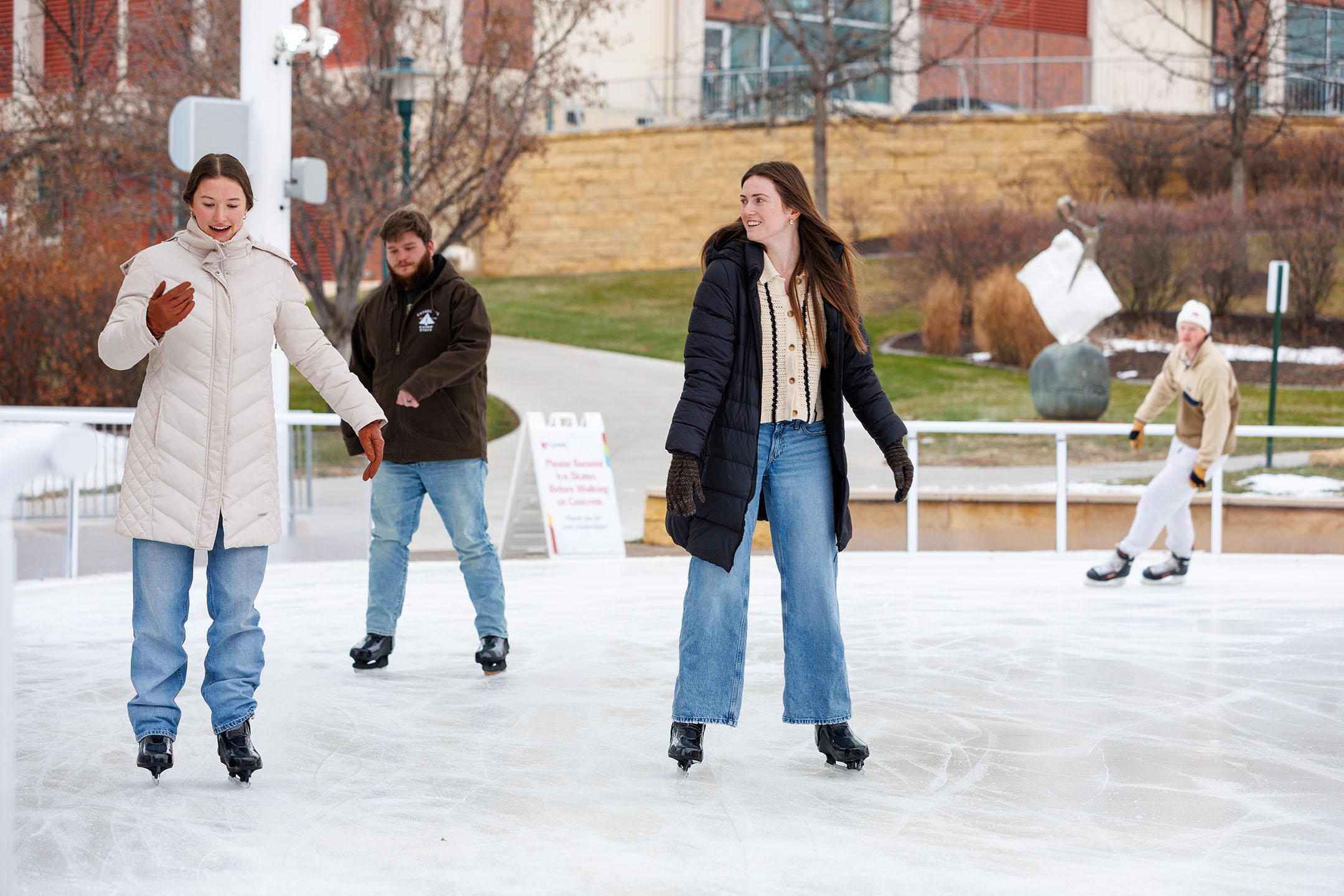 Two women ice skating in the foreground with two men ice skating in the background