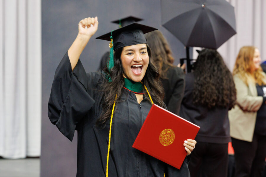 A UNMC graduate holding her new diploma raises her arm in celebration