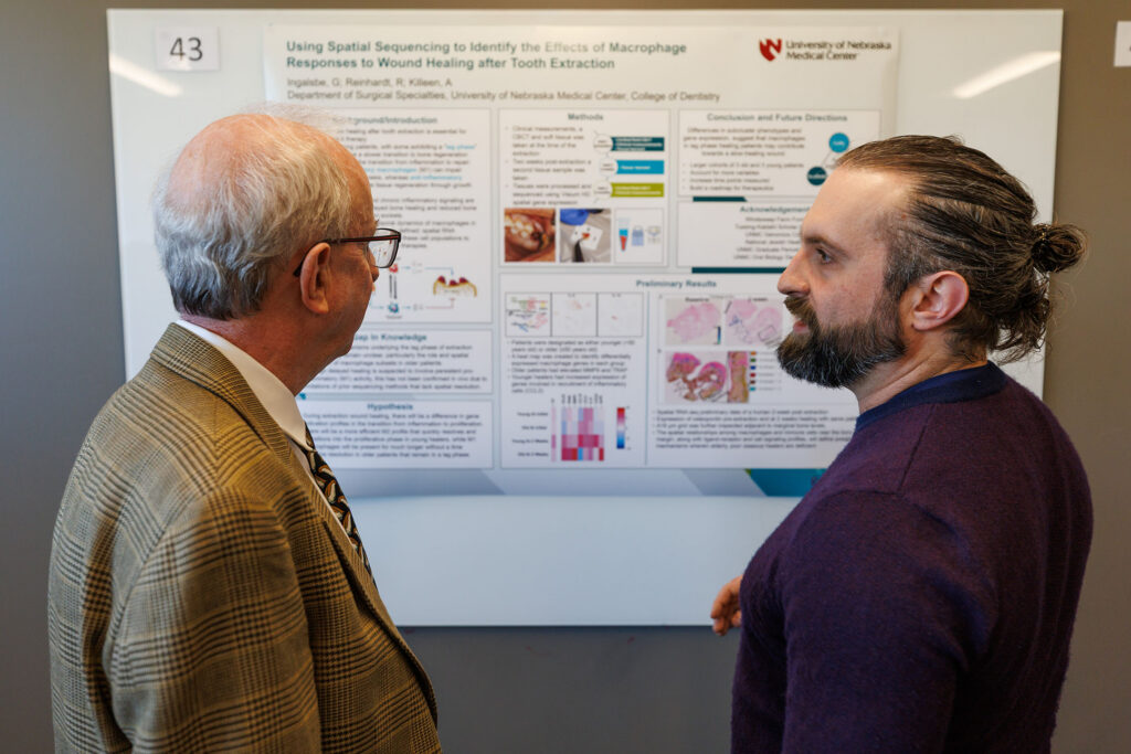 A dental student stands in front of his research board discussing his findings with a professor.