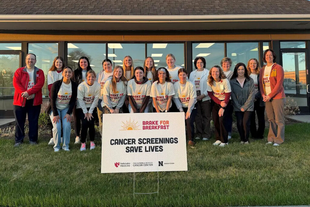 Photograph of a group of 19 people behind a sign that reads "Brake for Breakfast: Cancer Screenings Save Lives."