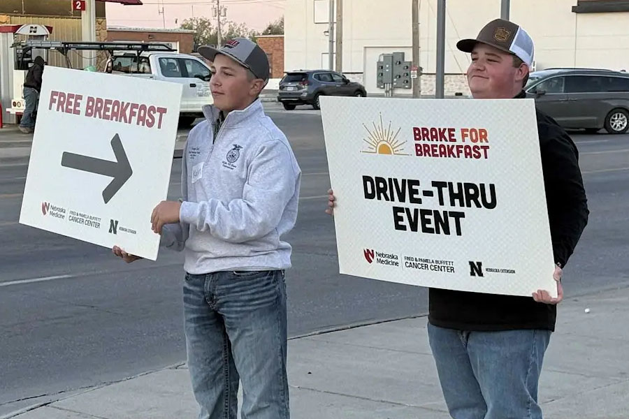 Photograph of a person holding a large sign with bold red text "FREE BREAKFAST" and a black right-pointing arrow. Sign includes logos for Nebraska Medicine, Fred & Pamela Buffett Cancer Center, and Nebraska.