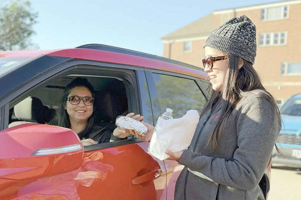 Photograph showing a person in a red car receiving a food item from a Brake for Breakfast volunteer.