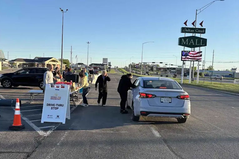 Photograph of a drive-thru stop setup in a parking lot near a mall, where volunteers hand out cancer screening information to people in cars.