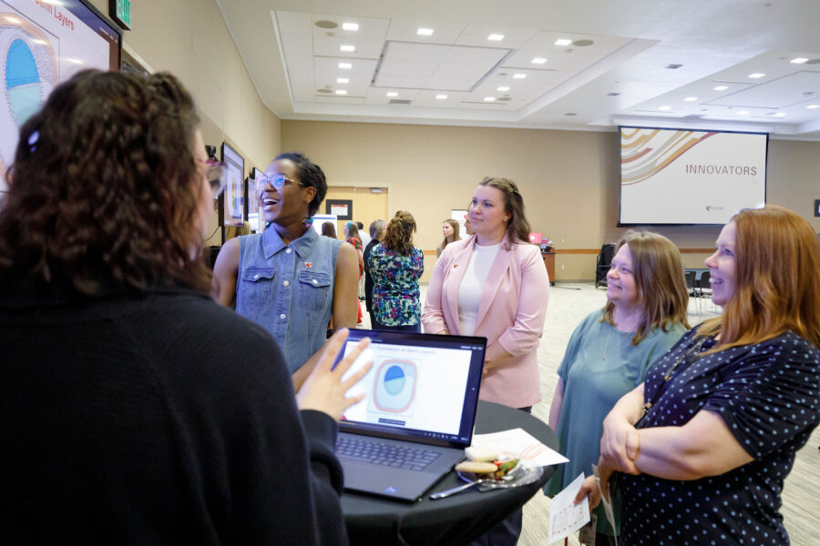 A group of four women stand around a research presenter at the UNMC E-Learning Showcase