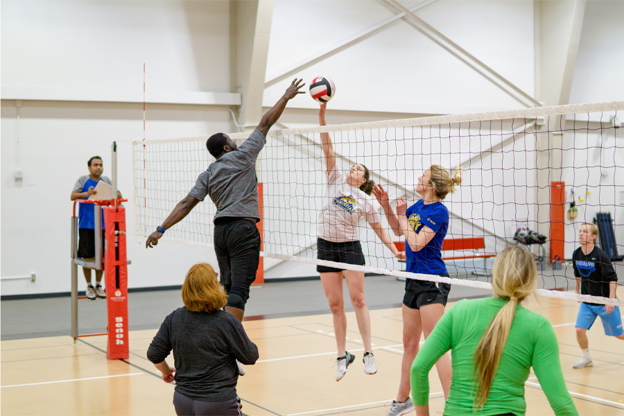 Image of UNMC students playing intramural volleyball, as a woman tries to hit the volleyball over the net and a man jumps to block.