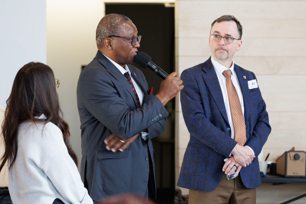 At the North Omaha Leadership Breakfast, UNMC Interim Chancellor H. Dele Davies, MD, stands to speak in front of the meeting, with Nebraska Medicine CEO Michael Ash, MD, in the right of the picture and Rachael Schmidt of the Fred & Pamela Buffett Cancer Center in the left of picture.