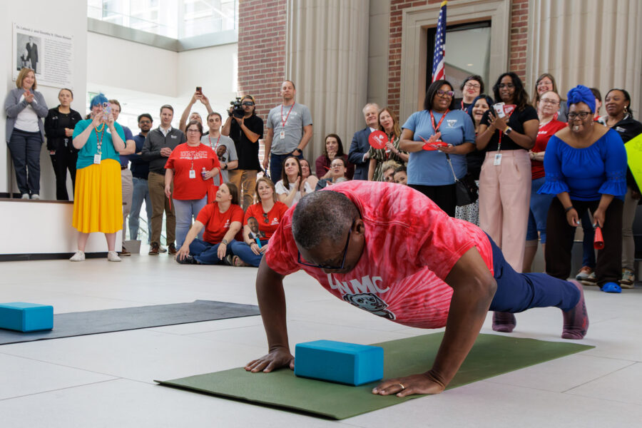 UNMC Interim Chancellor H&period; Dele Davies&comma; MD&comma; performs one of his 78 pushups during Wednesday's Chancellor's Push-Up Challenge during the For the Greater Good event&period; In the background&comma; supporters of the UNMC College of Public Health cheer on Dr&period; Davies &mdash; the college won the spirit awardin the background&period;