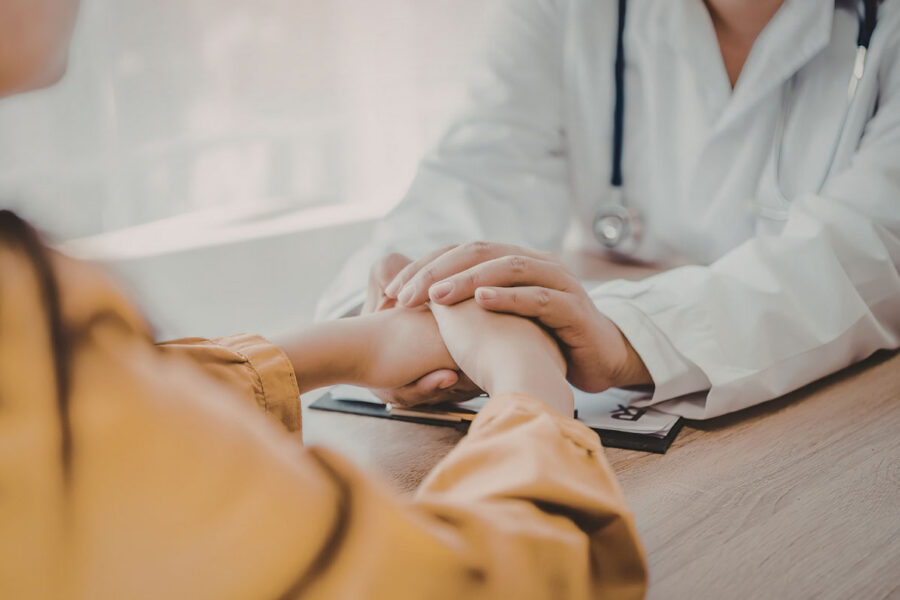 A healthcare professional holds hands in a clinical setting with a woman at the clinic, signifying support for a caregiver.