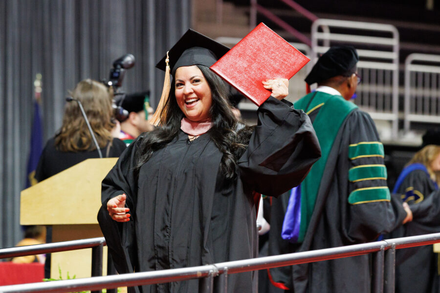 A UNMC graduate holds up her degree and smiles.