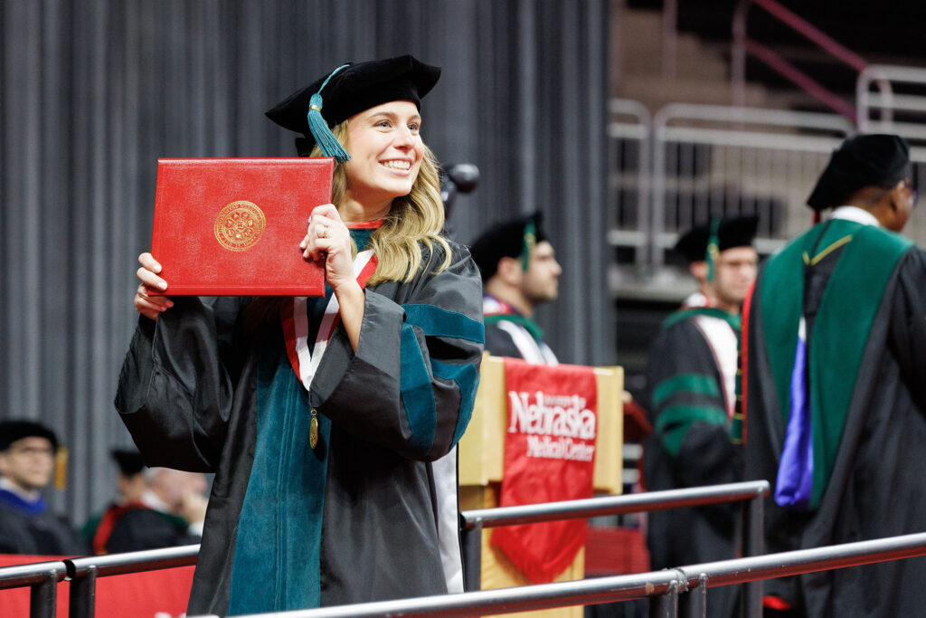 A graduate who just received her degree holds it up and smiles. University of Nebraska Medical Center spring commencement was held Saturday May 9, 2026, at Baxter Arena.