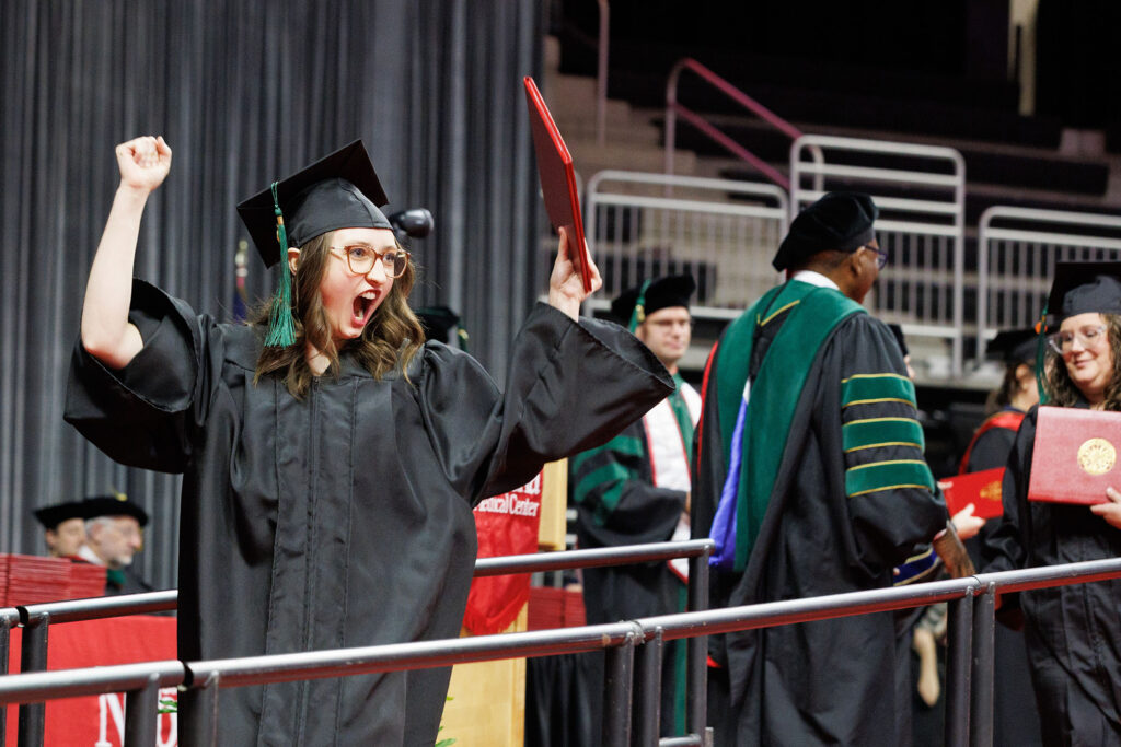 A graduate who just received her degree holds up her arms and opens her mouth to cheer. University of Nebraska Medical Center spring commencement was held Saturday May 9, 2026, at Baxter Arena.