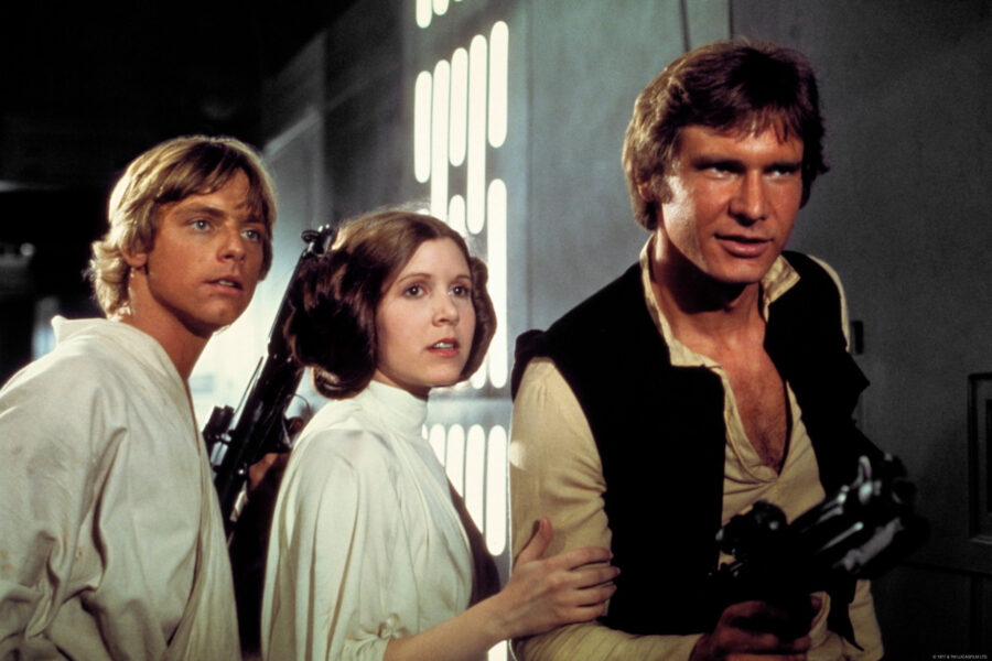 Star Wars heroes, from left, Luke Skywalker, Princess Leia and Han Solo stand next to each other and face to the right of frame in a scene from the movie.