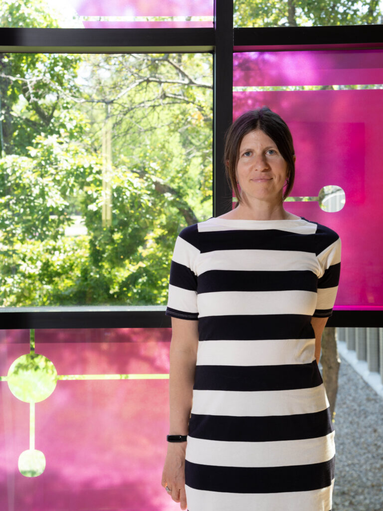 Artist Ann Tarantino, is a black and white horizontal-striped dress, stands in front of one of the window panes that make up "Field Trip," her artwork at the UNMC College of Dentistry.