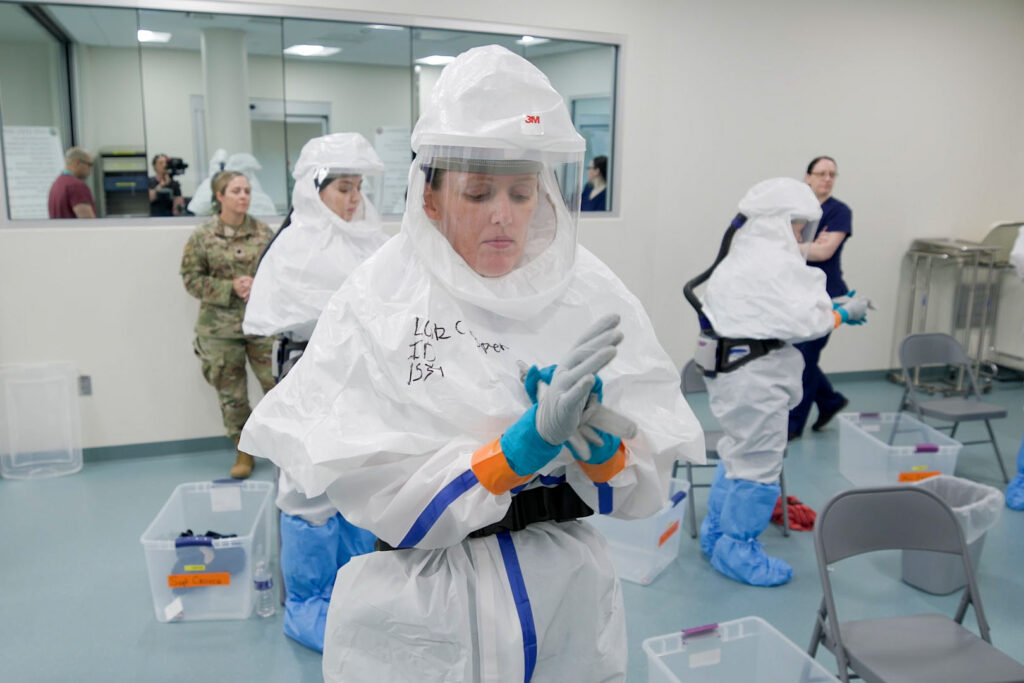 A medical professional from the Center for Sustainment of Trauma and Readiness Skills (C-STARS) Omaha, in full personal protective equipment, mops the floor while another team member tends to a simulated patient at the University of Nebraska Medical Center, June 14, 2024. The C-STARS Omaha team mobilized within 48 hours to provide specialized biocontainment care and medical monitoring for passengers exposed to the rare Andes virus. C-STARS Omaha is a unique Air Force training site specializing in infectious disease preparedness and biocontainment, ensuring medical teams are ready to respond to high-consequence diseases worldwide. (Screengrab taken from U.S. Air Force video by Ryan Law)