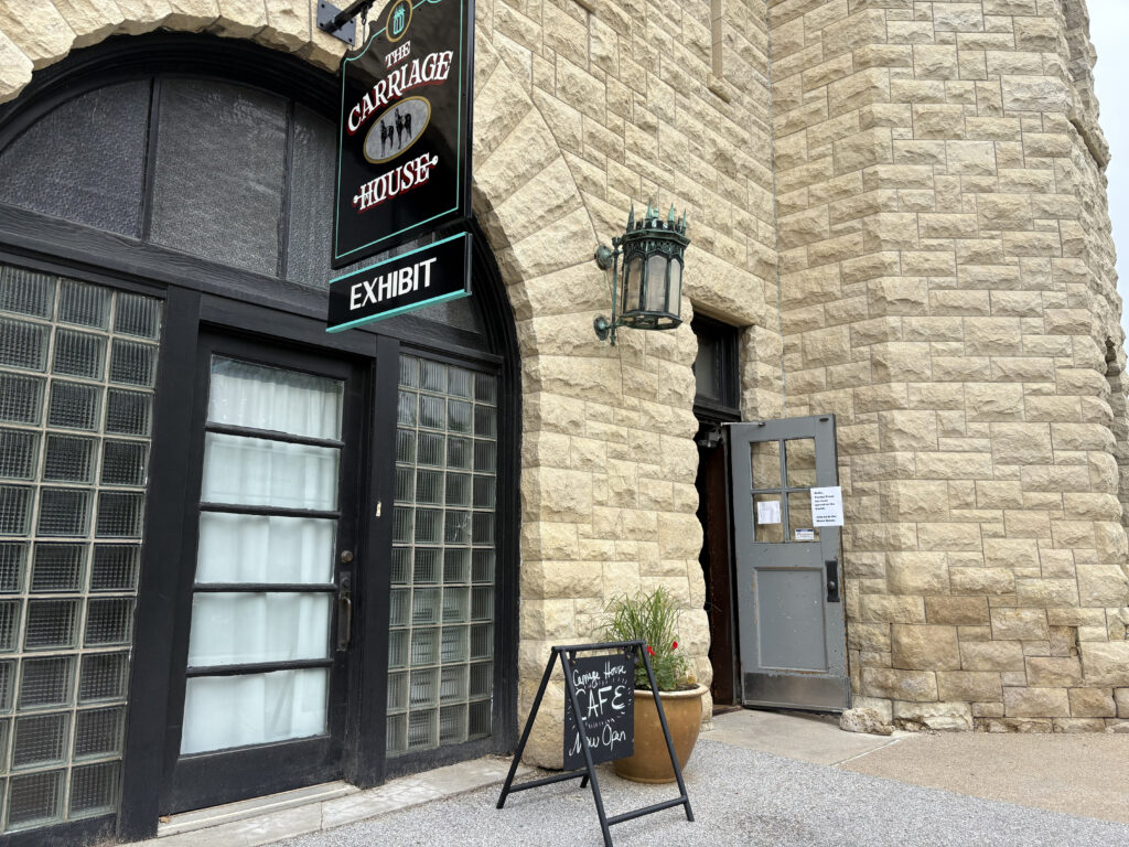 A Carriage House sign hangs on the building. A sign on the ground announces the Carriage House Cafe is now open.