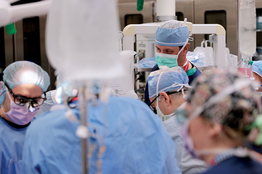 Surgical team in blue scrubs and masks focuses intently on a procedure. The operating room is busy, conveying a sense of urgency and concentration.