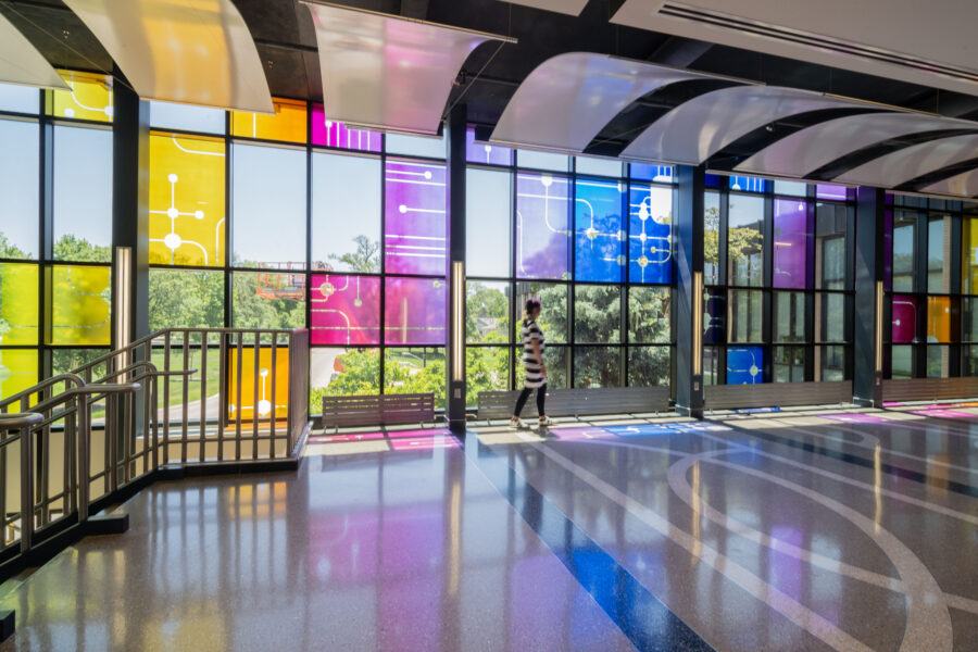 Artist Ann Tarantino crosses in front of her artwork "Field Trip" in the atrium of the UNMC College of Dentistry&comma; as the sunlight streaming through the windows casts colors such as blue&comma; purple and yellow on the atrium floor&period;