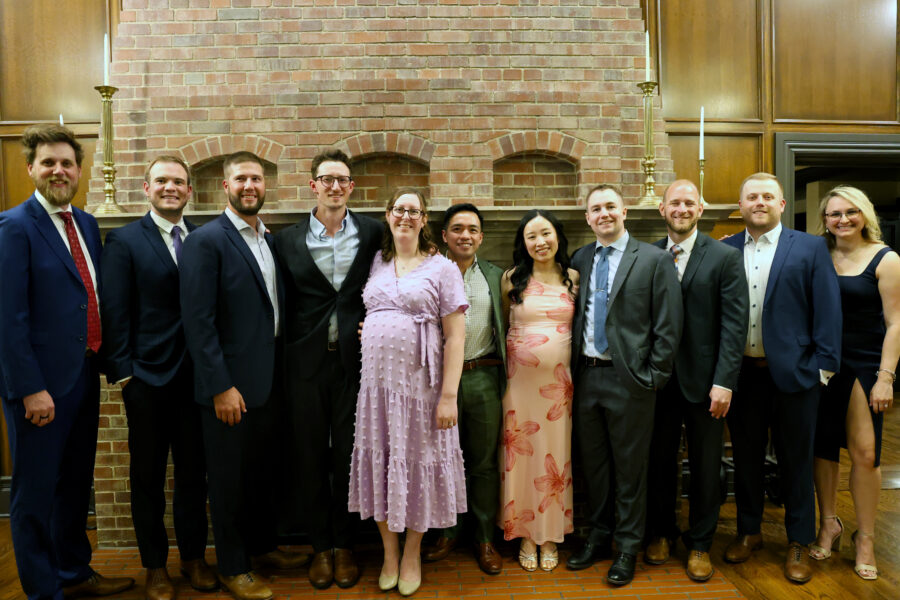 Eleven graduates from the anesthesiology graduation pose together in front of a fireplace at Omaha Country Club.