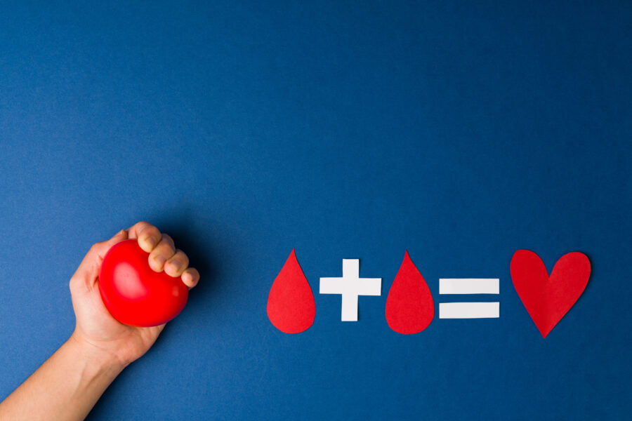 On a blue field, a fist grips a foam heart. To the right of it, there is an equation: a red drop of blood + a red drop of blood = a red heart