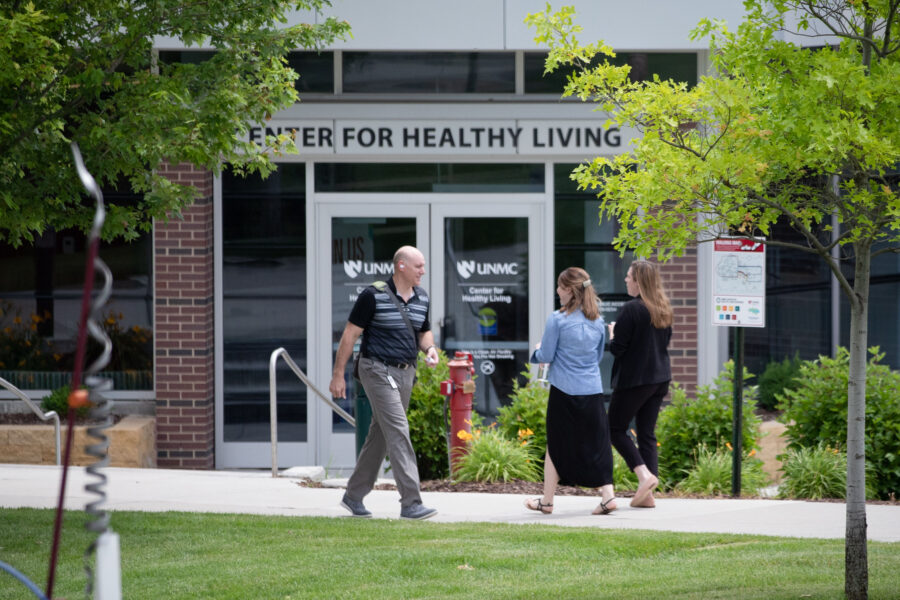Foot traffic outside the UNMC Center for Healthy Living, with a tall man walking past two smaller women headed in the opposite direction.