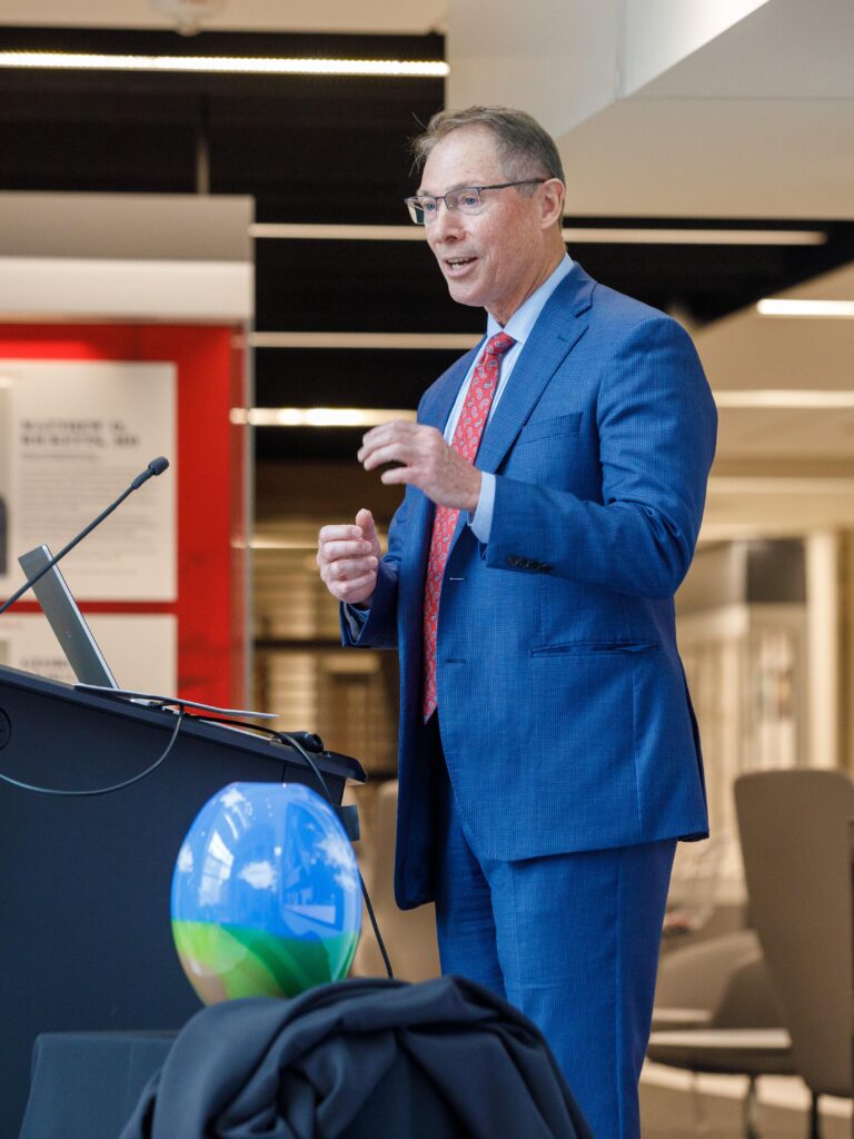 Kyle Meyer, PhD, speaks in front of a podium, holding his hands at chest height as he talks through a smile.