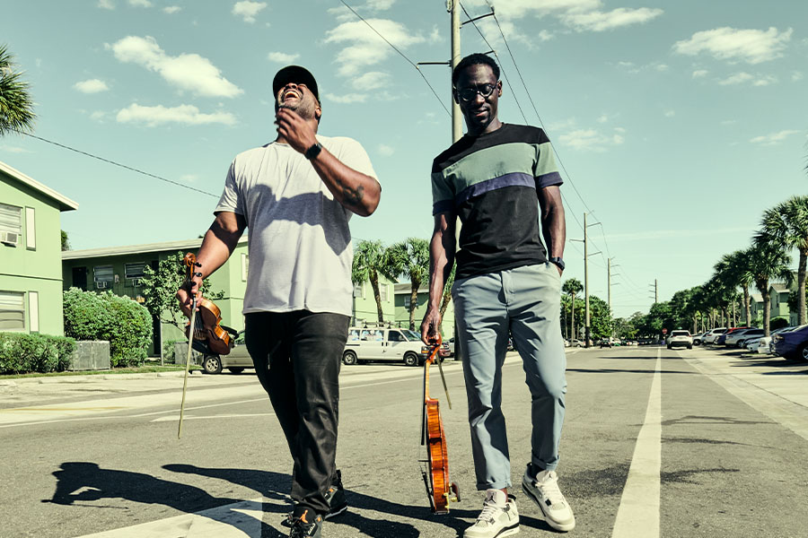 Members of the musical group Black Violin walk down a street, one with his head throw nack in laughter