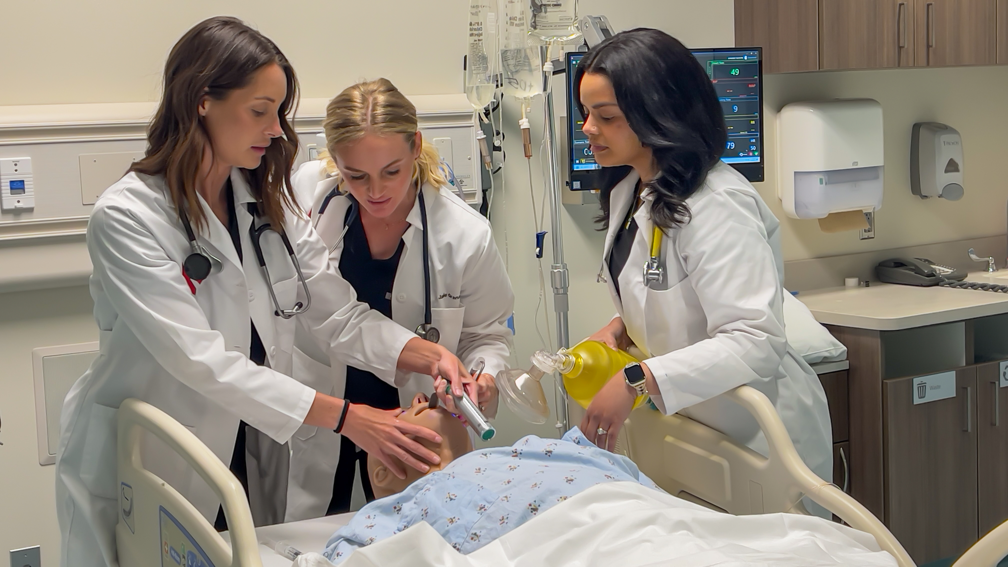 Three people do an emergency drill on a simulation manikin.