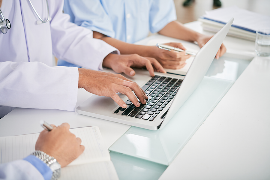 View of three people's hands at a white desk, notepad, and laptop.