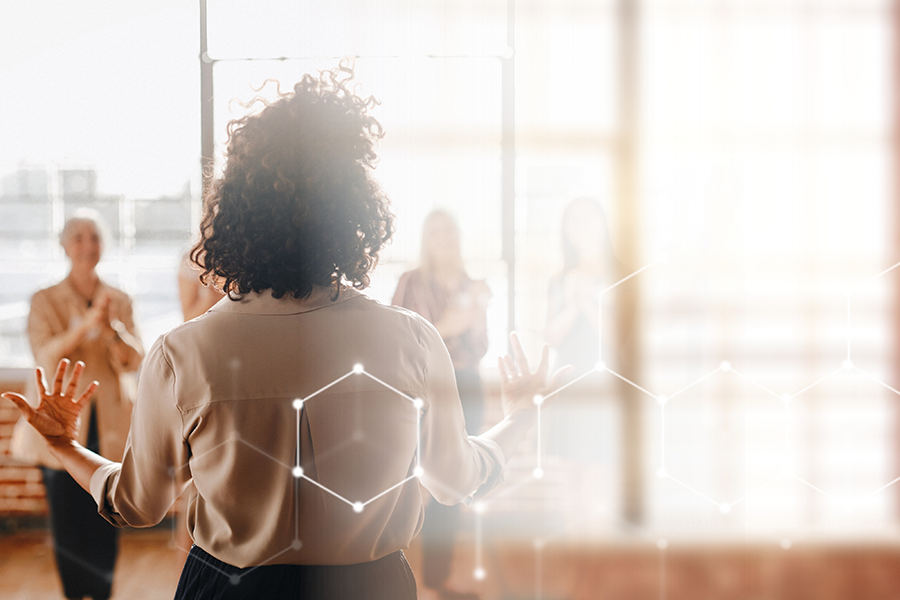Woman with back turned, arms raised part way, and women standing in background  and right side of photo lighter and blurry.