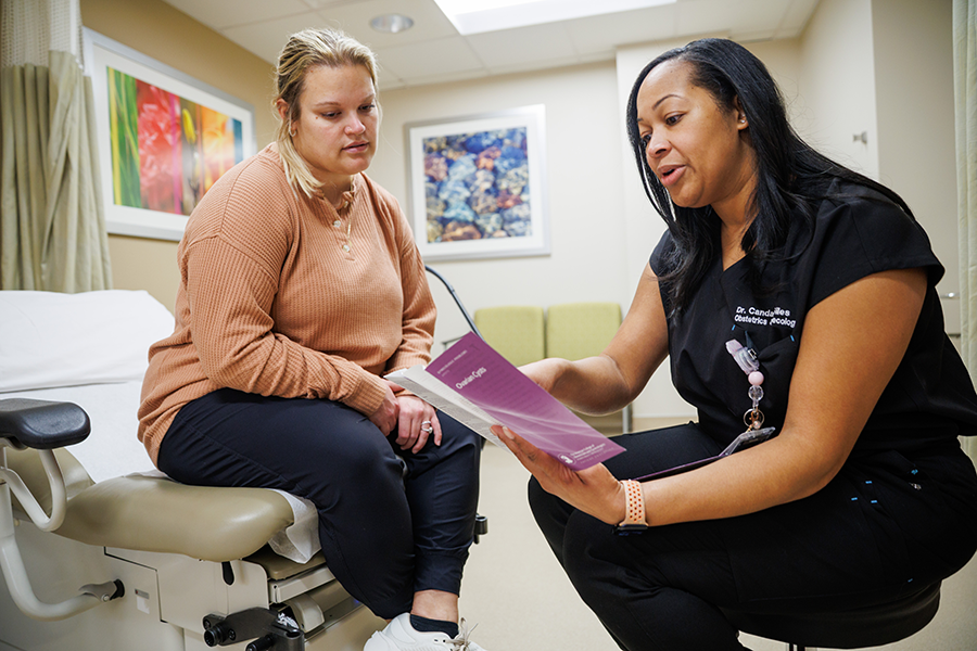 Patient sitting on an exam table and physician wearing black scrubs, discussing information in a pamphlet.