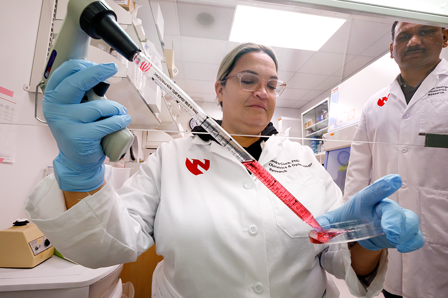 Kendra Clark, PhD, holds a pipelle under a venting hood and applies red liquid into a petri dish.