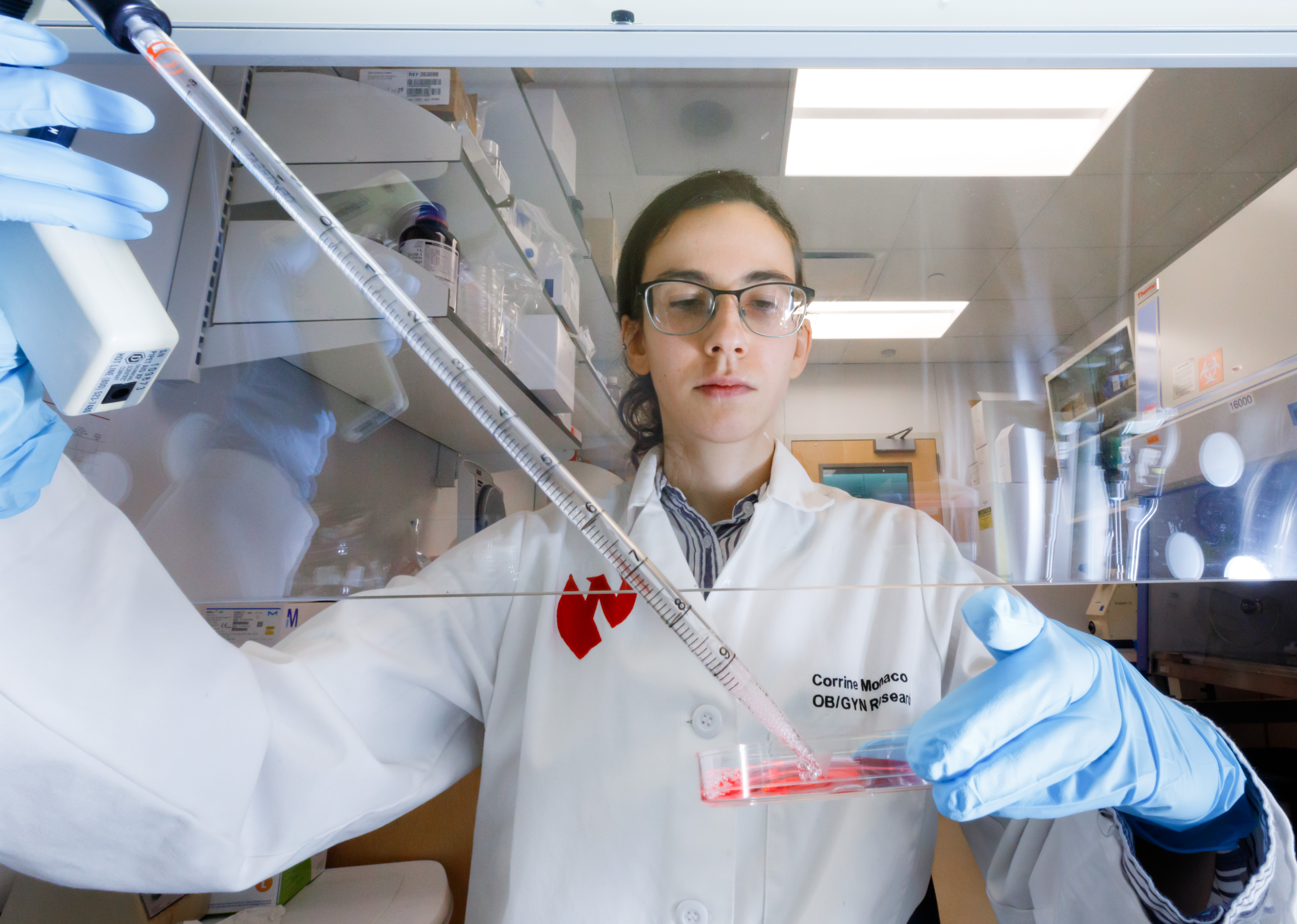 Corrine Monaco holds a pipelle under a venting hood and applies red liquid into a petri dish.