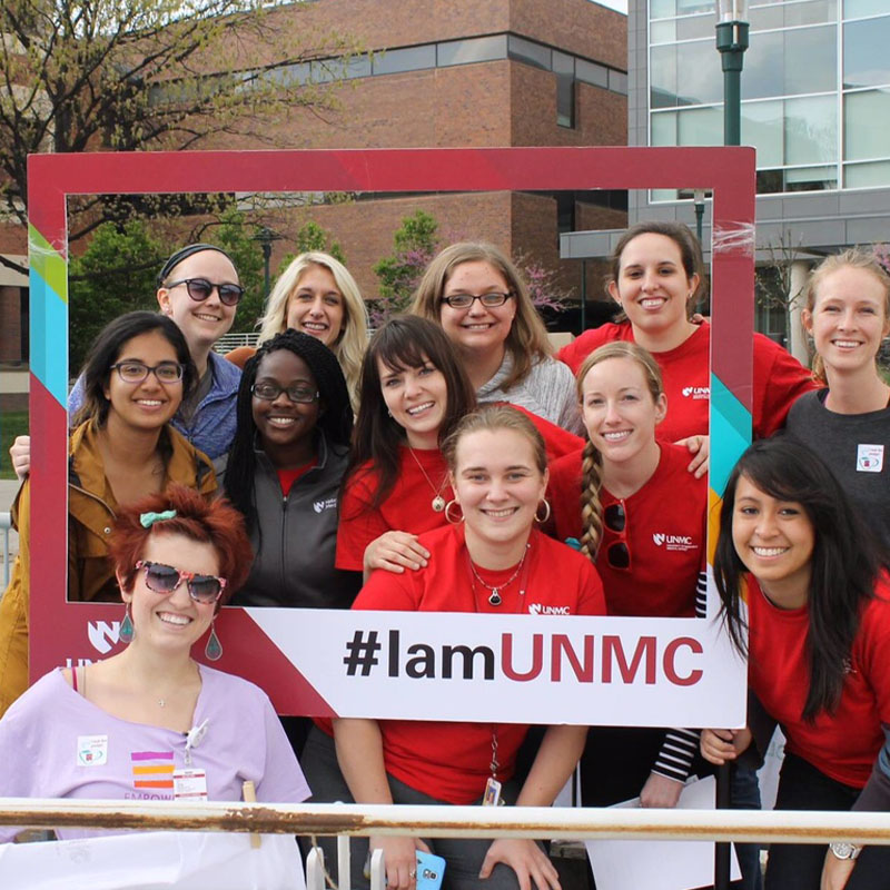 Students stand in a group posing for a shot holding an empty picture frame