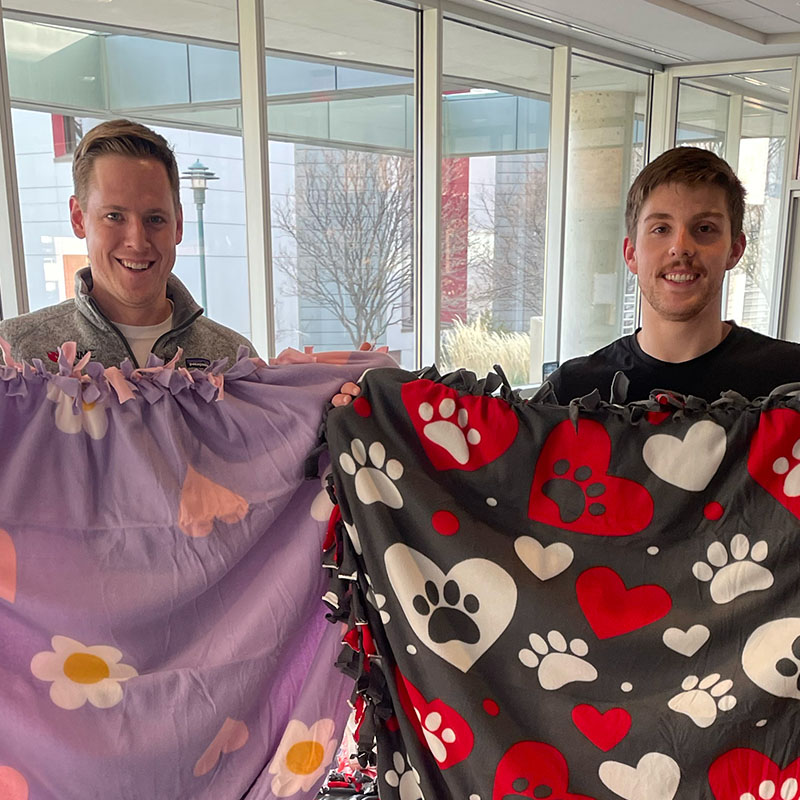 Four students hold up blankets they made for community members